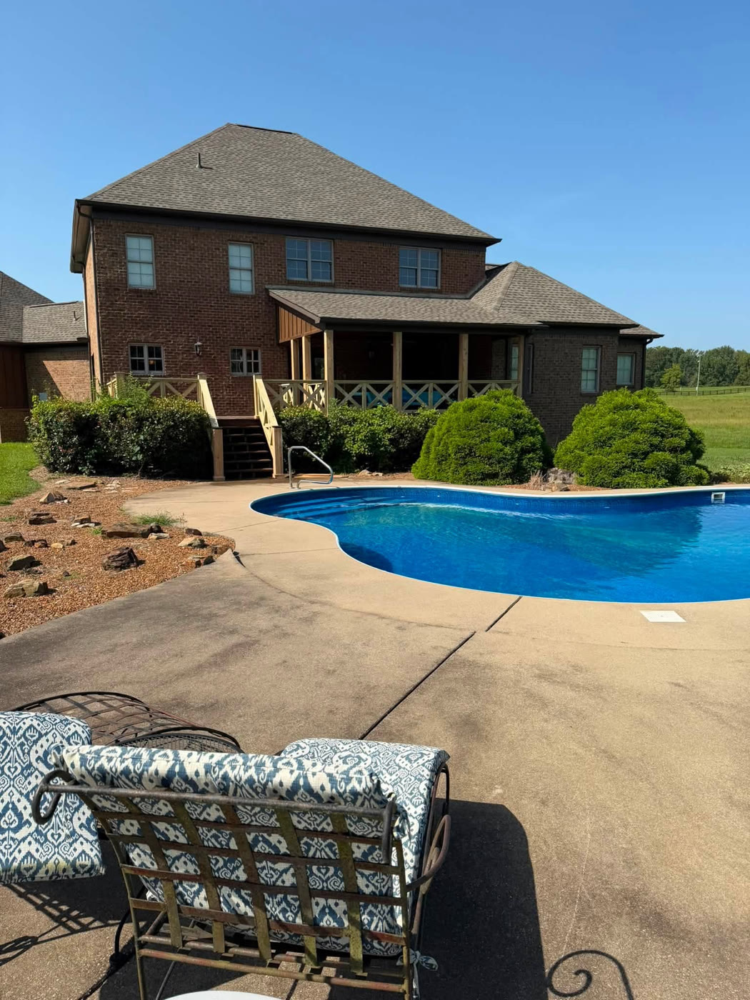 Brick home with new wooden X-rail deck and covered porch overlooking an in-ground pool