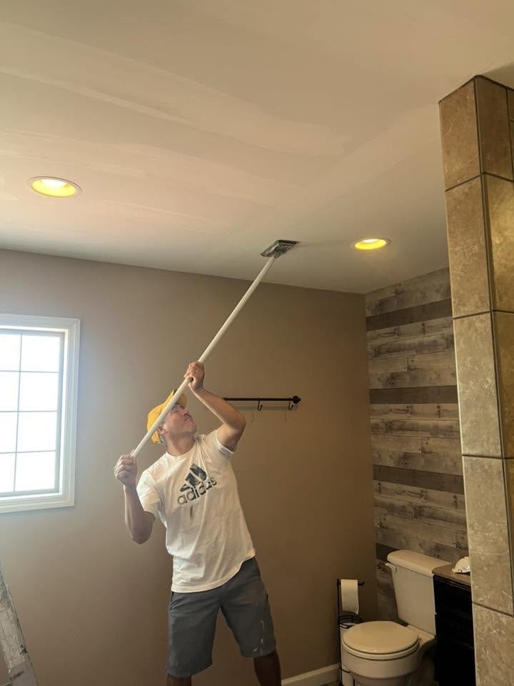 Worker sanding drywall ceiling joints in a bathroom under renovation