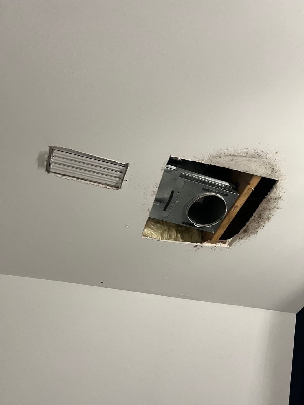 Bathroom ceiling with installed air vent and open cutout showing HVAC unit and framing