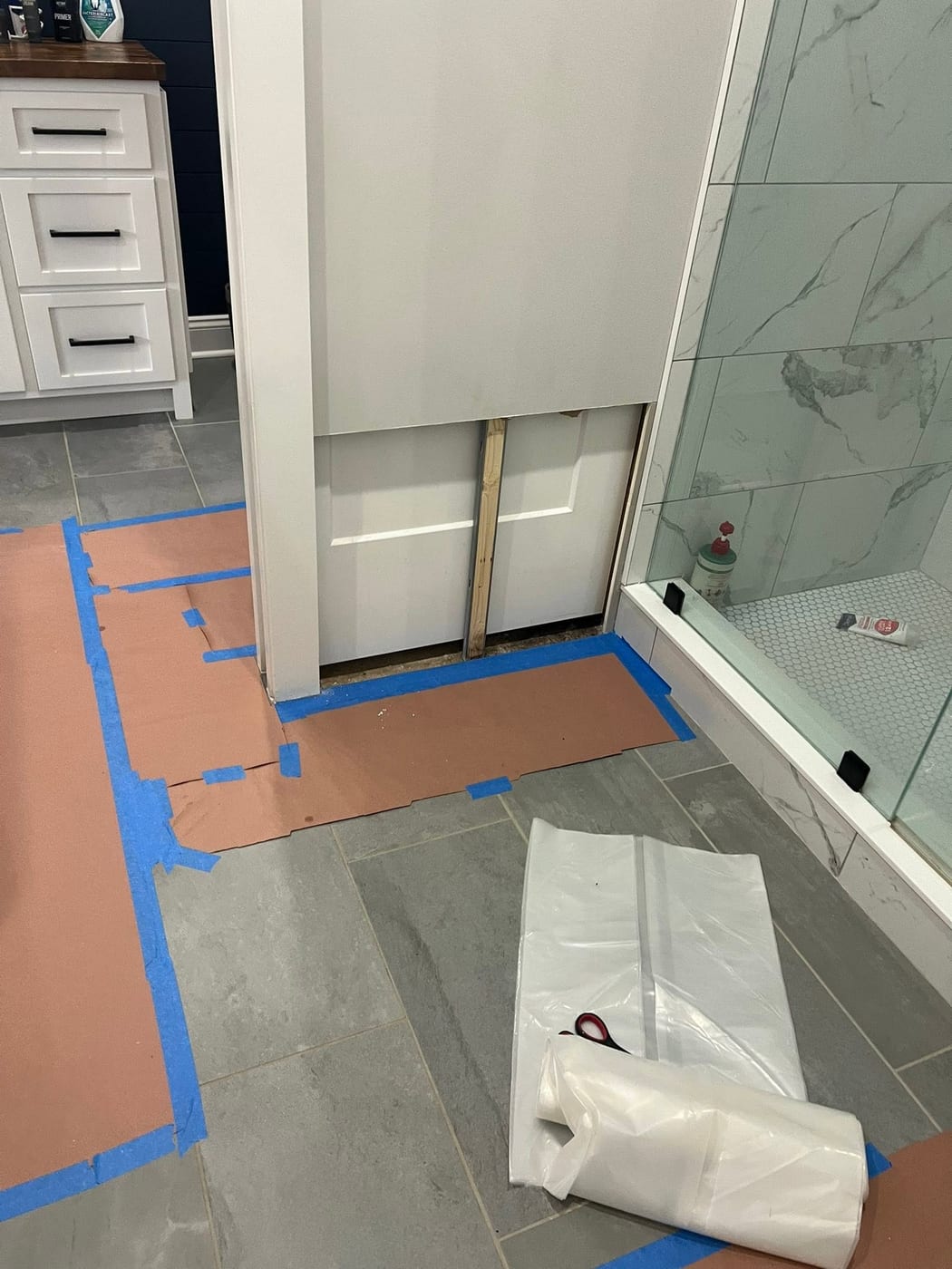 White pocket door being installed beside a marble-tiled walk-in shower