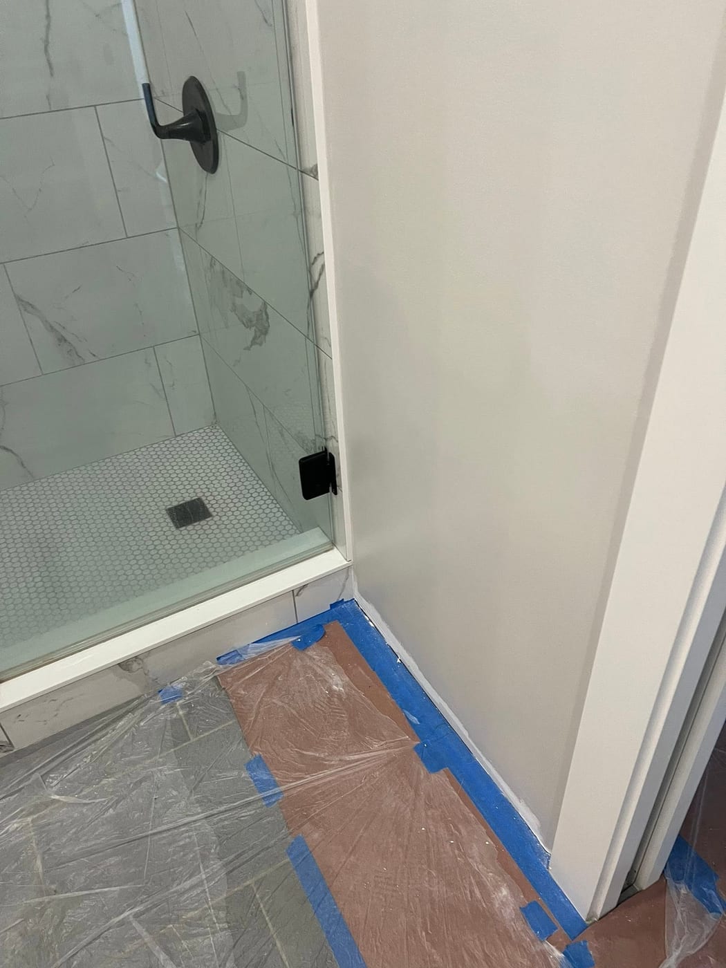 Walk-in shower with marble-pattern wall tile, white hexagonal floor tile, and matte black hardware