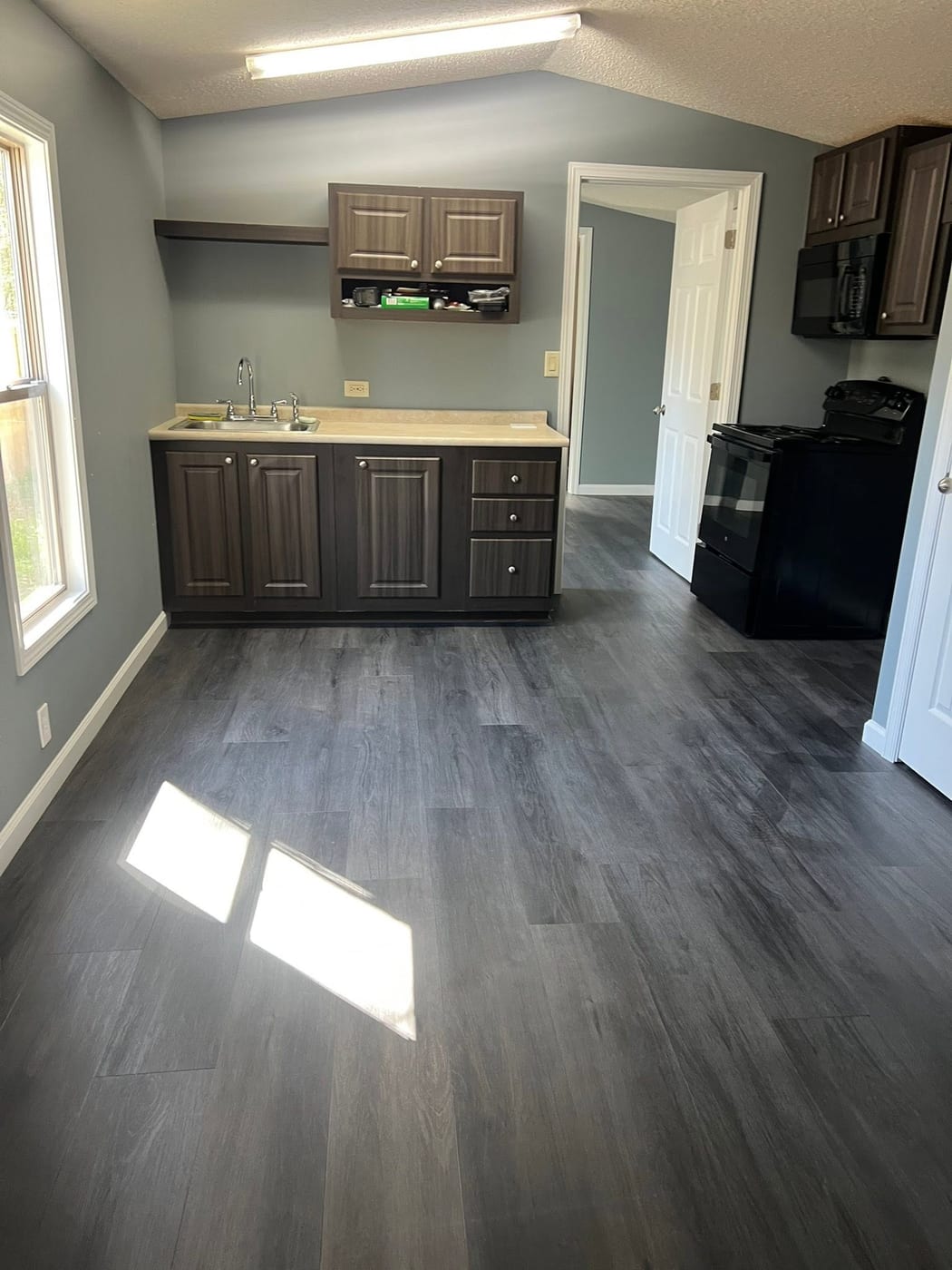 Finished kitchenette with grey wood-look flooring, blue-grey walls, dark cabinets, and white trim