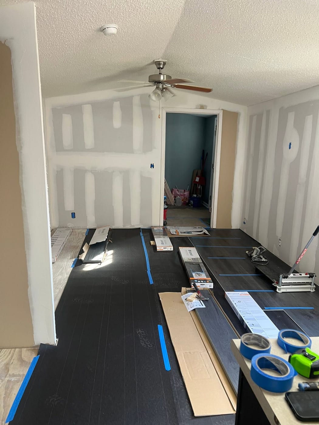 Room in progress with taped drywall seams and new wood-look flooring being installed over underlayment